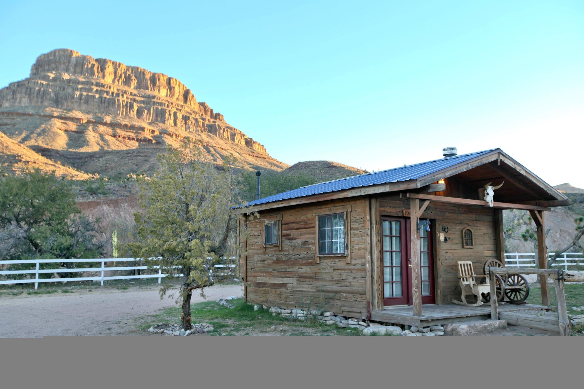 A pine cabin with a porch standing below the red bulk of Spirit Mountain at dawn