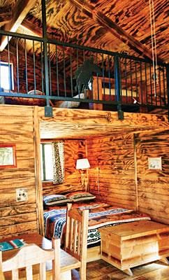 Cabin interior looking up to the sleeping loft, with beds and a wooden rail