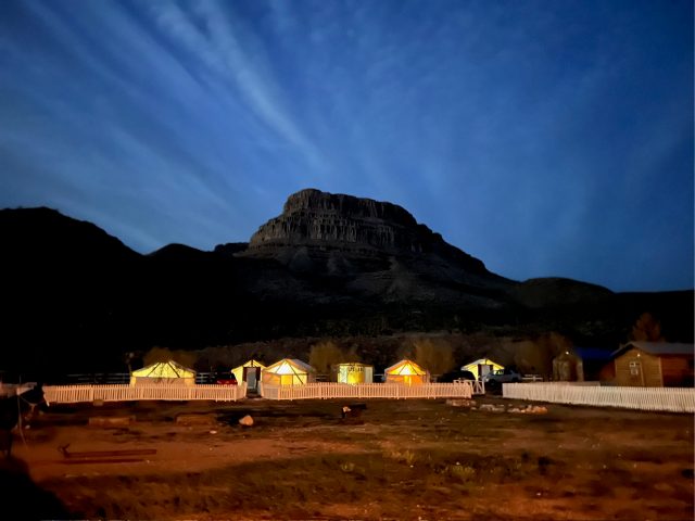 A row of lit glamping tents below the mesa at dusk
