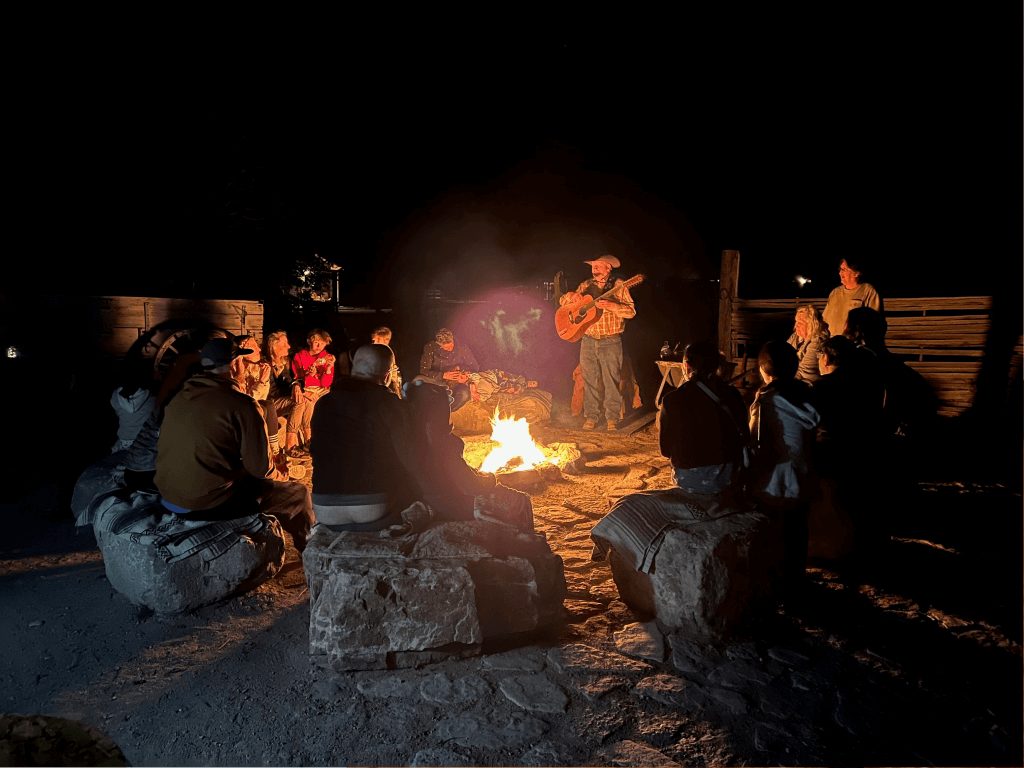 Guests sitting on blankets around a large open campfire at the ranch after dark
