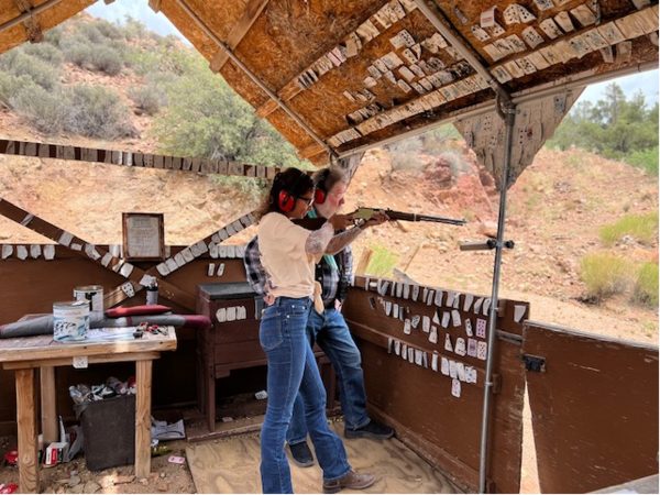 A guest shooting a lever-action rifle from a covered bench at the ranch gun range